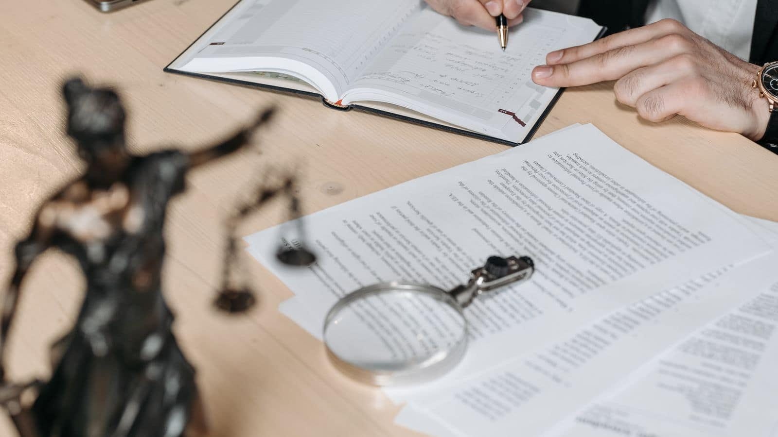 Documentos legales, lupa y figura de la justicia sobre la mesa de un despacho