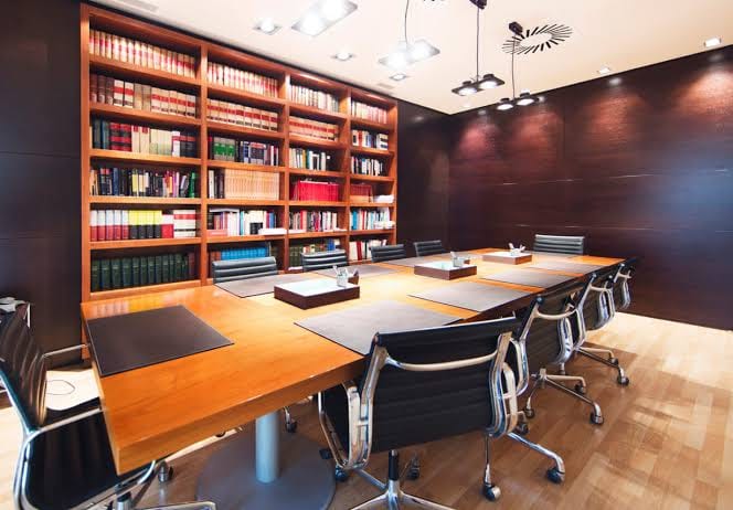 Sala de reuniones de un despacho de abogados, con mesa larga y librería de códigos legales
