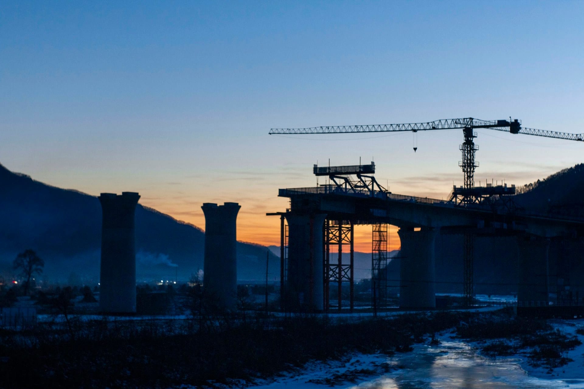 Viaducto en construcción con una grúa torre al atardecer